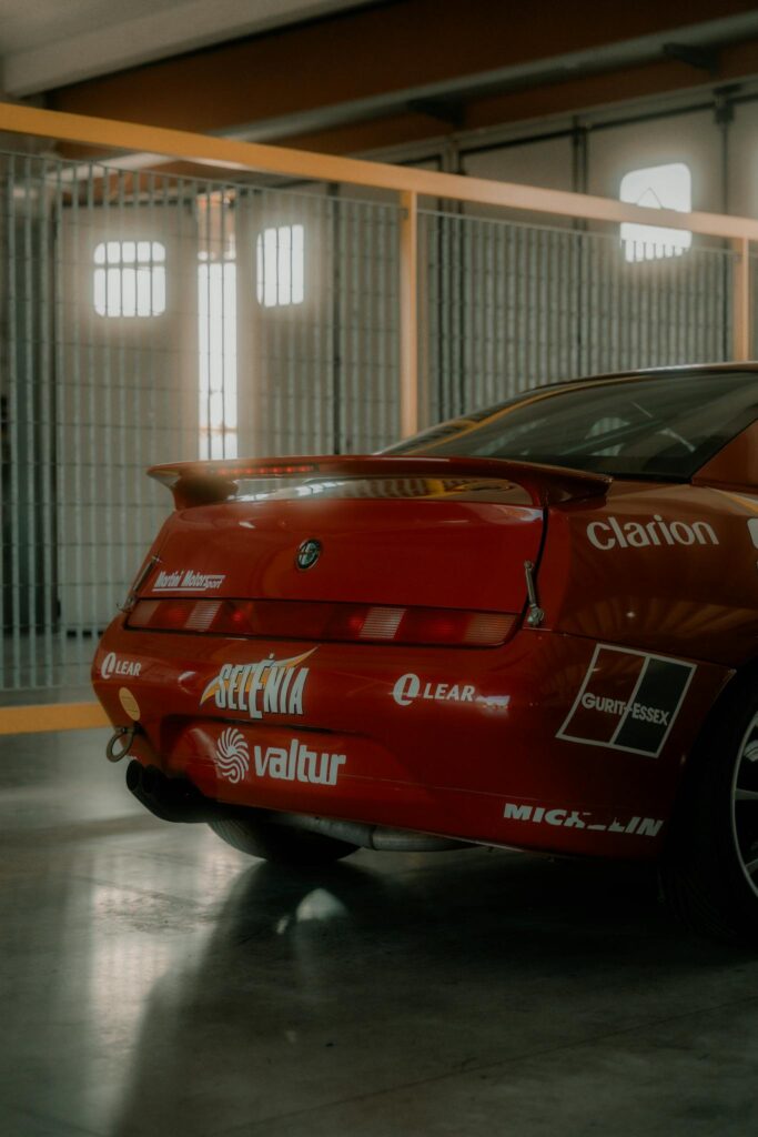 A sleek red Alfa Romeo touring car with branding in an indoor setting. Perfect for motorsport enthusiasts.