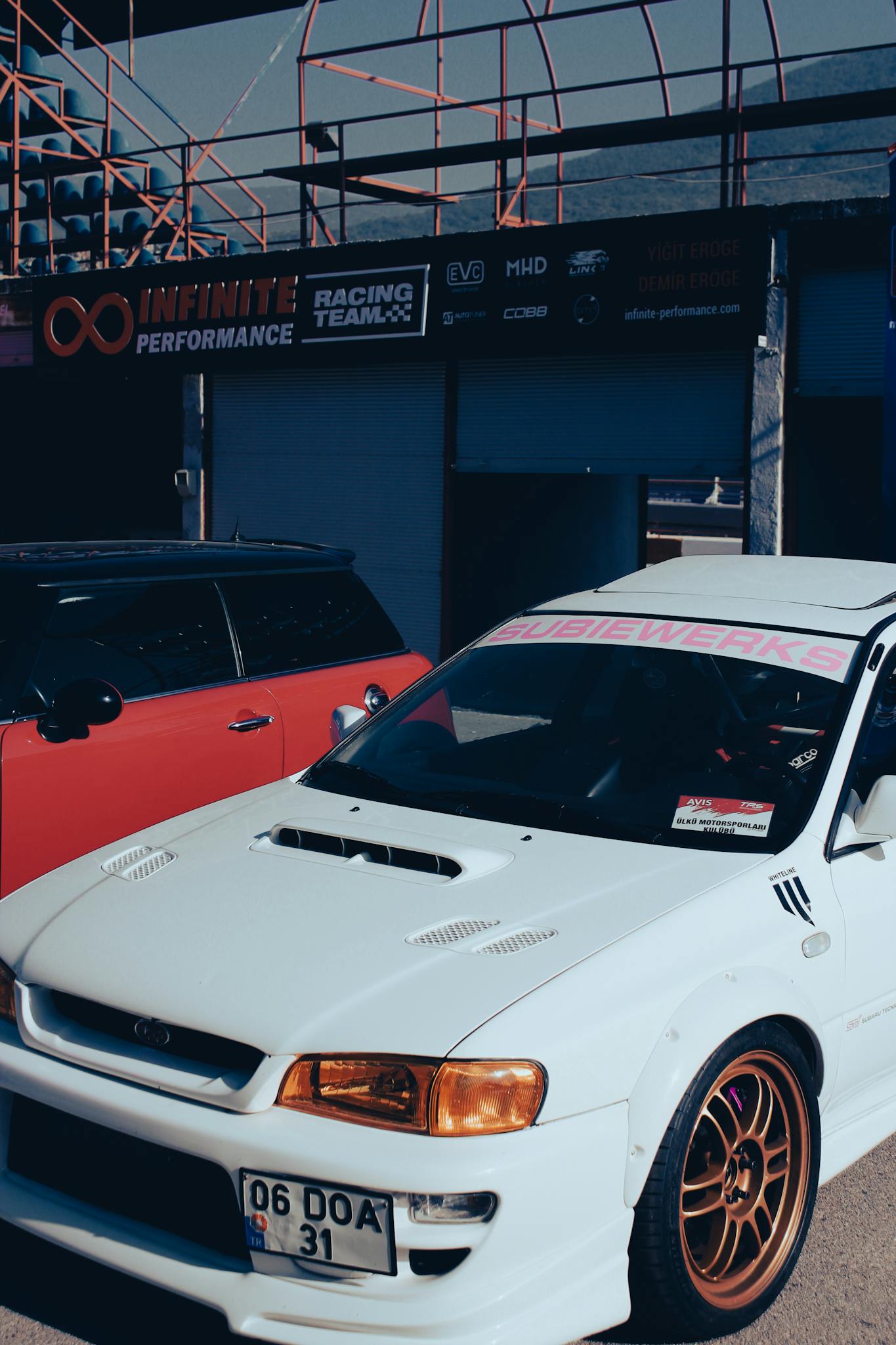 A sleek white racing car parked outdoors at a motorsport event during the day.